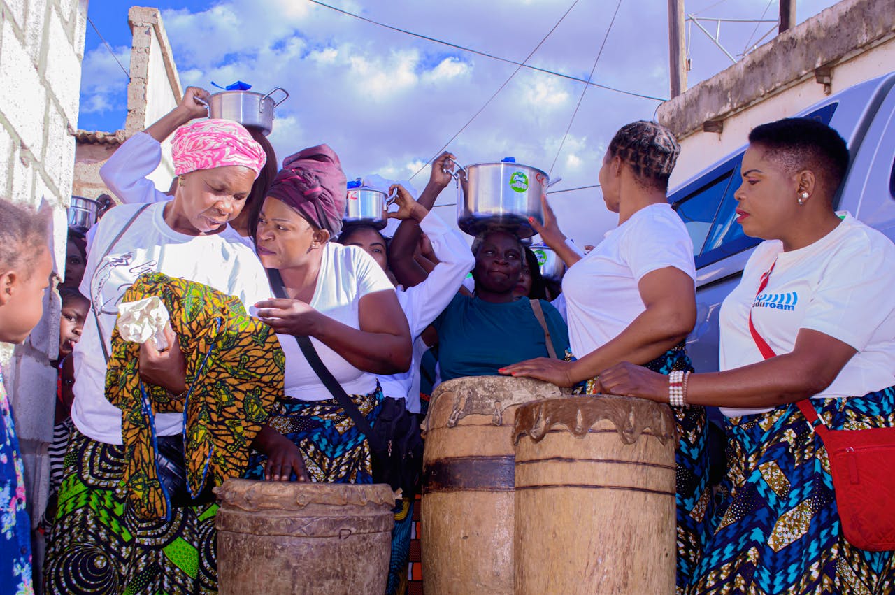 about-01 A lively group of women celebrating with music and traditional drumming outdoors.