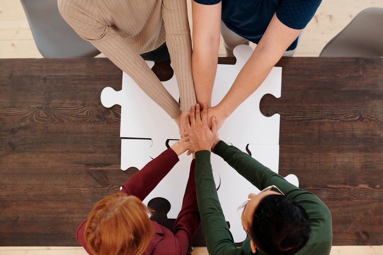 gallery-2 Engaging image of diverse people's hands coming together on puzzle pieces, symbolizing unity.