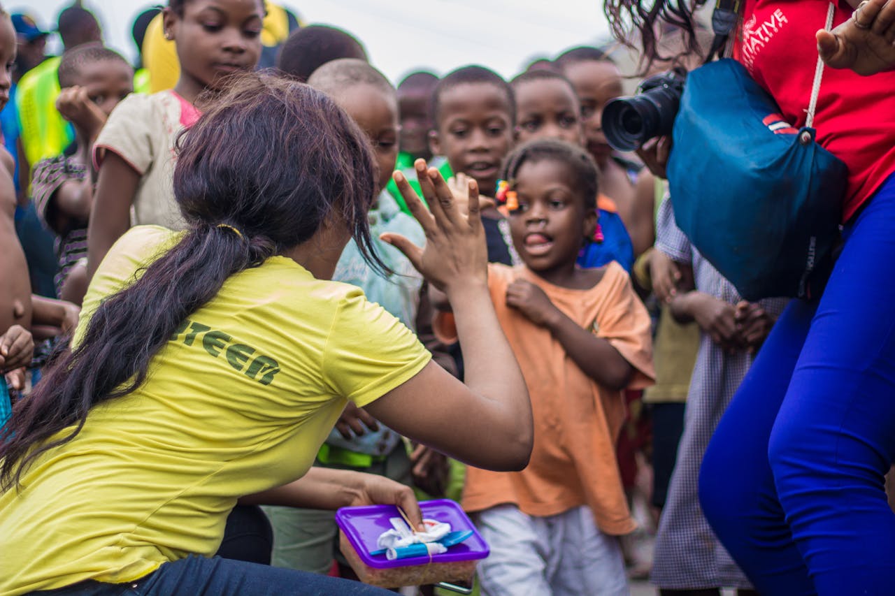 why-choose-us A woman engages with children through a high-five in a vibrant community setting.