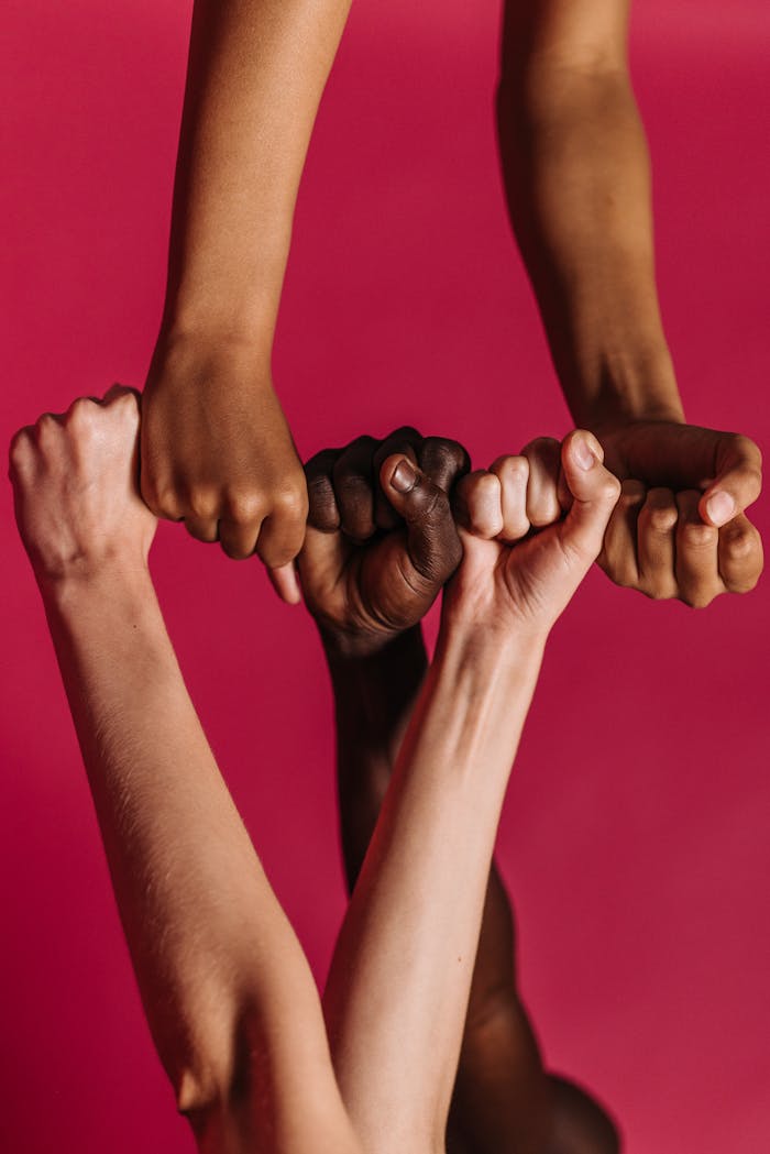 Four diverse arms join together in solidarity against a vibrant red backdrop.